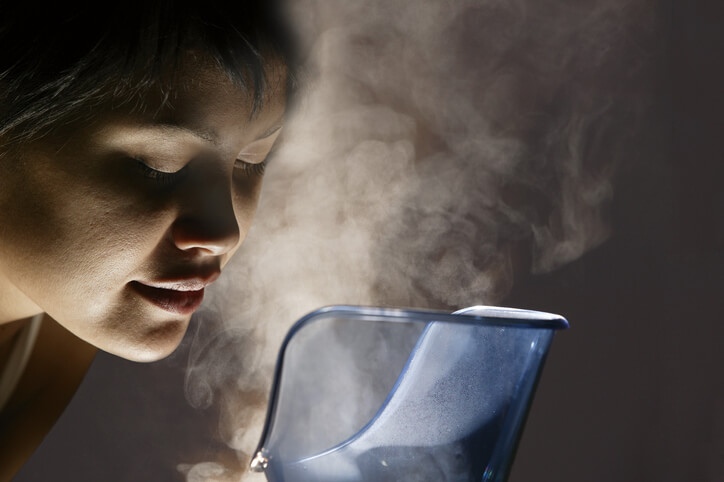 A woman breaths in the steam rising from a humidifier.